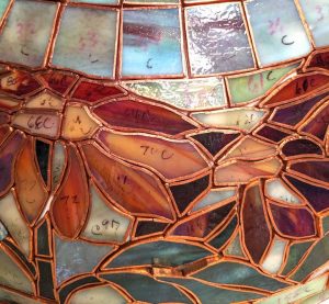 The edges of each piece of glass are wrapped in copper foil and affixed to the form with wax. 