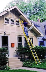 Man on ladder removing aluminum overhang.