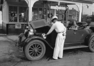 Woman sitting in old car while a man fills it with gas