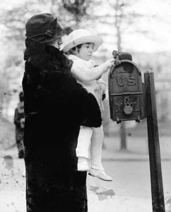 Mother holding a child who puts a letter in a mailbox