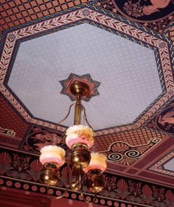 Photo of light hanging from a decorated ceiling.
